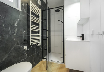 Baño moderno en blanco y negro en Eco Lodge, con ducha, radiador toallero y diseño elegante y minimalista.