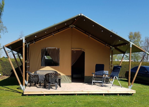 Safari-Zelt auf De Scherpenhof in den Niederlanden mit Terrasse, Tischen und Stühlen unter blauem Himmel.