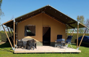 Tienda tipo safari en De Scherpenhof, Países Bajos, con terraza, mesas y sillas bajo un cielo despejado.