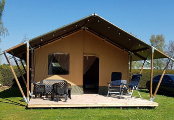 Safari-Zelt auf De Scherpenhof in den Niederlanden mit Terrasse, Tischen und Stühlen unter blauem Himmel.