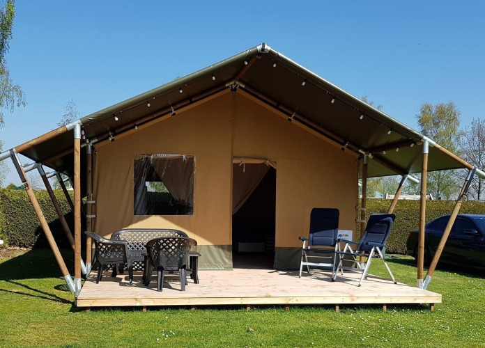 Tienda tipo safari en De Scherpenhof, Países Bajos, con terraza, mesas y sillas bajo un cielo despejado.