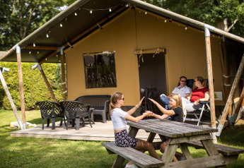 Familia relajándose fuera de una tienda safari en De Scherpenhof, Países Bajos; niños jugando en mesa.
