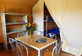 Interior de tienda safari en De Scherpenhof con mesa, sillas, estantería, flores y literas visibles.