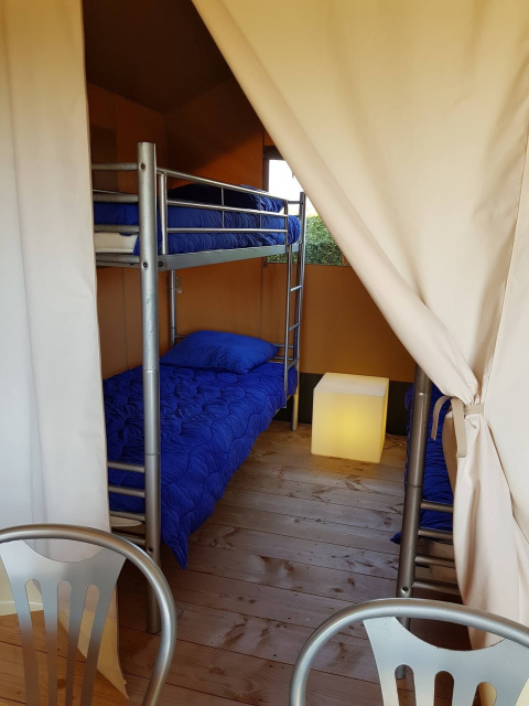 Vista interior de una tienda safari con literas y ropa de cama azul en De Scherpenhof, Países Bajos.