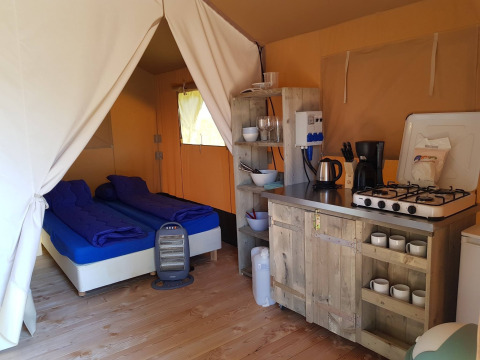 Vista interna di una tenda safari a De Scherpenhof, Paesi Bassi, con letti, cucina e dotazioni da campeggio.