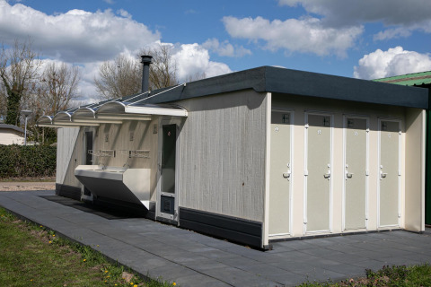 Edificio sanitario exterior con puertas de baño separadas y lavabos en la tienda Safari de De Scherpenhof, Países Bajos.