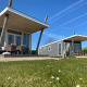 Zwei moderne Strandhäuser mit Terrassenmöbeln auf Camping Zonneweelde, Niederlande, unter blauem Himmel.