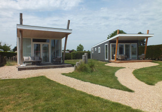 Dos casas diminutas modernas llamadas Beach Loft en Camping Zonneweelde, Países Bajos, rodeadas de césped.