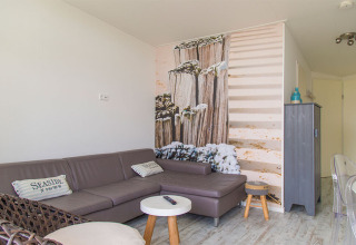Piccolo soggiorno nel Beach Loft a Camping Zonneweelde con divano grigio e murale a tema spiaggia.