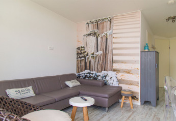 Petit salon du Beach Loft au Camping Zonneweelde avec canapé gris et fresque murale sur le thème de la plage.