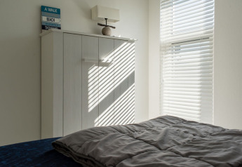 La lumière du soleil à travers les stores projette des rayures sur une armoire dans une chambre lumineuse du Beach Loft.