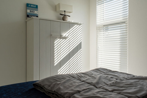Zonnestralen door jaloezieën creëren strepen op een kast in een lichte slaapkamer in Beach Loft, Camping Zonneweelde.