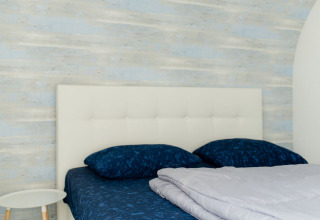 Lichte slaapkamer met blauw beddengoed en wit hoofdbord in Beach Loft, Camping Zonneweelde, Nederland.