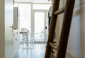 Kikker gennem en entré med træstige til et køkken og spiseplads i Beach Loft, Camping Zonneweelde, Holland.