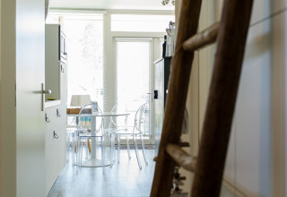 Zicht door gang met houten ladder richting keuken en eetruimte in Beach Loft, Camping Zonneweelde, Nederland.