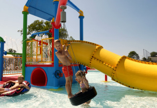 Des enfants jouent dans un parc aquatique coloré avec toboggan lors d’un séjour glamping en plein air.