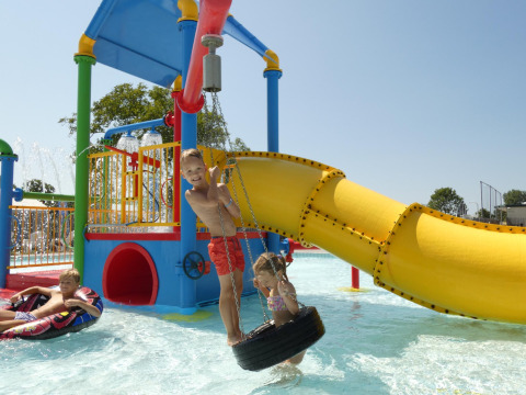 Niños jugando en un parque acuático colorido con tobogán y flotadores en un alojamiento glamping.