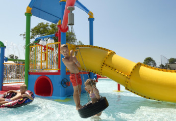 Niños jugando en un parque acuático colorido con tobogán y flotadores en un alojamiento glamping.
