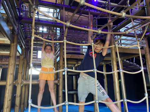 Twee kinderen spelen vrolijk op een touwladder in een glampingverblijf met houten constructie.