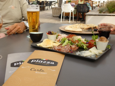 Comida al aire libre en glamping, con menú, bebidas, aperitivo y comensales sentados en la mesa.