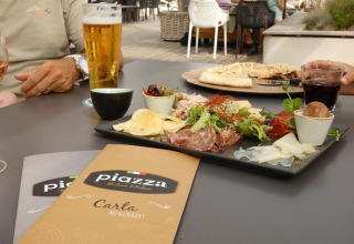 Pranzo all'aperto in un glamping, con menù, bevande, stuzzichini e ospiti seduti al tavolo.