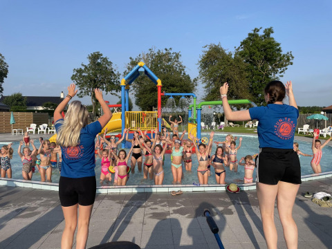 Niños jugando en una piscina guiados por dos monitores en un alojamiento glamping soleado.