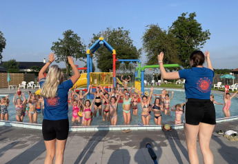 Niños jugando en una piscina guiados por dos monitores en un alojamiento glamping soleado.