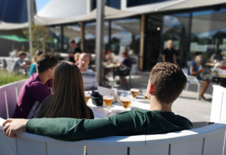 Cuatro jóvenes se relajan en la terraza de un alojamiento glamping, disfrutando bebidas al sol juntos.