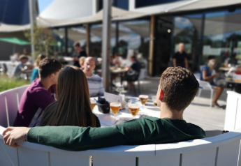 Quattro giovani si rilassano al bar esterno di un glamping, circondati da sole e atmosfera moderna.
