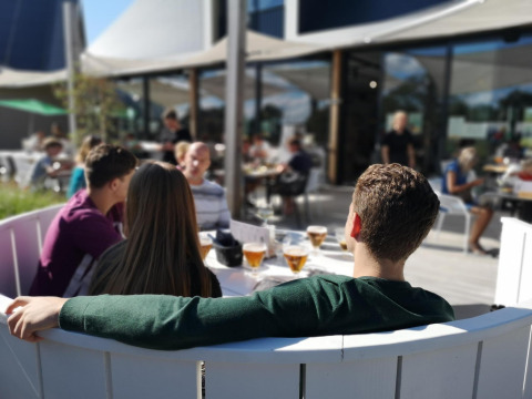 Cuatro jóvenes se relajan en la terraza de un alojamiento glamping, disfrutando bebidas al sol juntos.