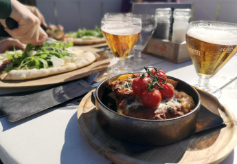 Udendørs frokost på glamping: pizza med rucola, gratinret og øl ved et solrigt bord.