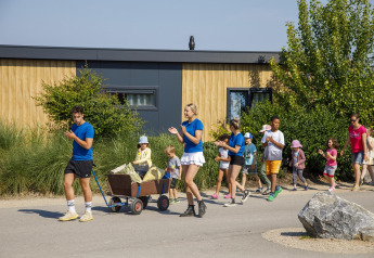 Enfants et adultes marchent et jouent devant une tiny house à Beach Loft, Camping Zonneweelde, Pays-Bas.