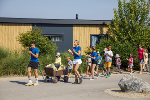 Bambini e adulti passeggiano e giocano vicino a una tiny house al Beach Loft nel Camping Zonneweelde, Paesi Bassi.