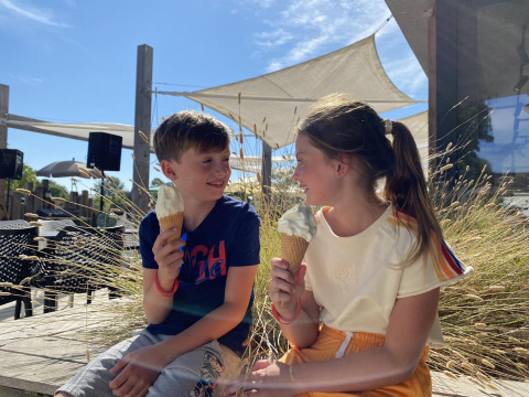 Dos niños disfrutan de helados frente a un alojamiento glamping moderno bajo el sol brillante.