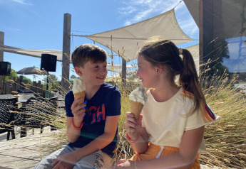 Dos niños disfrutan de helados frente a un alojamiento glamping moderno bajo el sol brillante.