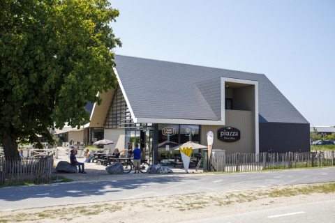 Modern glamping accommodation with a stylish wooden building, outdoor seating, and people enjoying the sun.