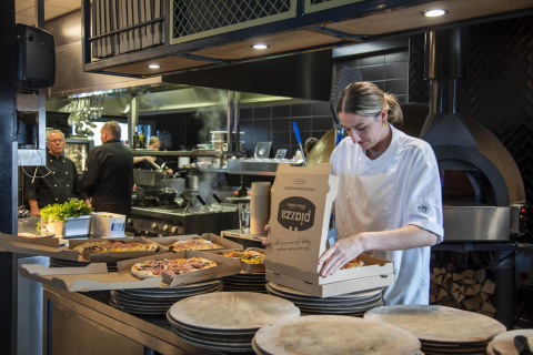 Chef con chaqueta blanca empaqueta pizzas en cajas en una cocina moderna en Beach Loft glamping.