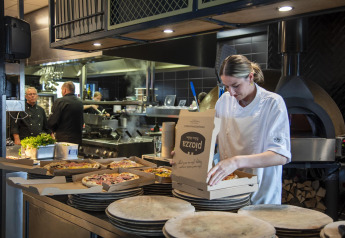 Chef con chaqueta blanca empaqueta pizzas en cajas en una cocina moderna en Beach Loft glamping.