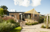 Exterior de Dune Lodge de Luxe en Camping Zonneweelde, con fachada moderna de madera y toldo solar.