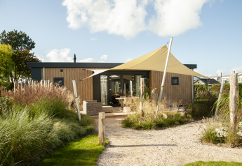 Außenansicht der Dune Lodge de Luxe auf Camping Zonneweelde mit moderner Holzoptik und Sonnensegel.