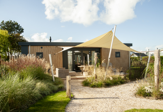 Außenansicht der Dune Lodge de Luxe auf Camping Zonneweelde mit moderner Holzoptik und Sonnensegel.