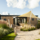 Exterior de Dune Lodge de Luxe en Camping Zonneweelde, con fachada moderna de madera y toldo solar.