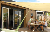 Familia toma café en la terraza de Dune Lodge de Luxe en Camping Zonneweelde, Países Bajos, en un día soleado.