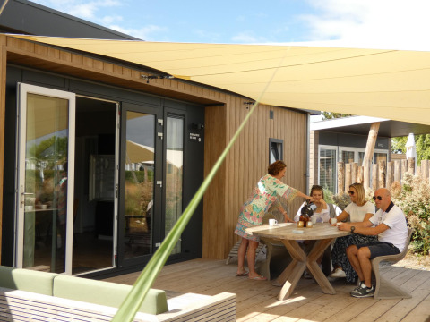 Familia toma café en la terraza de Dune Lodge de Luxe en Camping Zonneweelde, Países Bajos, en un día soleado.