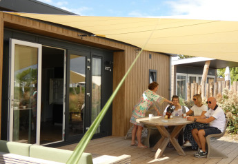 Gezin geniet van koffie op het terras bij Dune Lodge de Luxe op Camping Zonneweelde in Nederland, zomer.