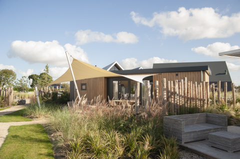 Zeitgemäße Dune Lodge de Luxe auf dem Camping Zonneweelde in den Niederlanden mit natürlicher Bepflanzung.