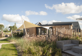 Moderne Dune Lodge de Luxe op Camping Zonneweelde in Nederland met houten buitenkant en tuin.