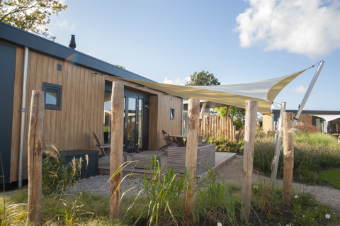 Buitenaanzicht van Dune Lodge de Luxe bij Camping Zonneweelde in Nederland met terras en schaduwdoek.