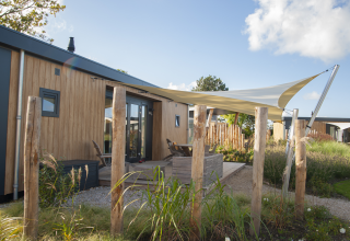 Vista exterior del Dune Lodge de Luxe en Camping Zonneweelde, Países Bajos, con terraza y toldo moderno.