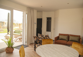Lichte en moderne leefruimte in Dune Lodge de Luxe op Camping Zonneweelde met zicht op het terras.